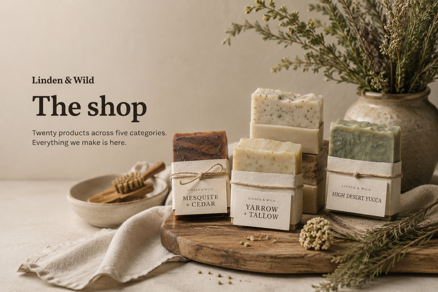 The shop: twenty products across five categories. Everything we make is here. Three soaps stacked on a wooden board, surrounded by dried botanicals and a stoneware jar.